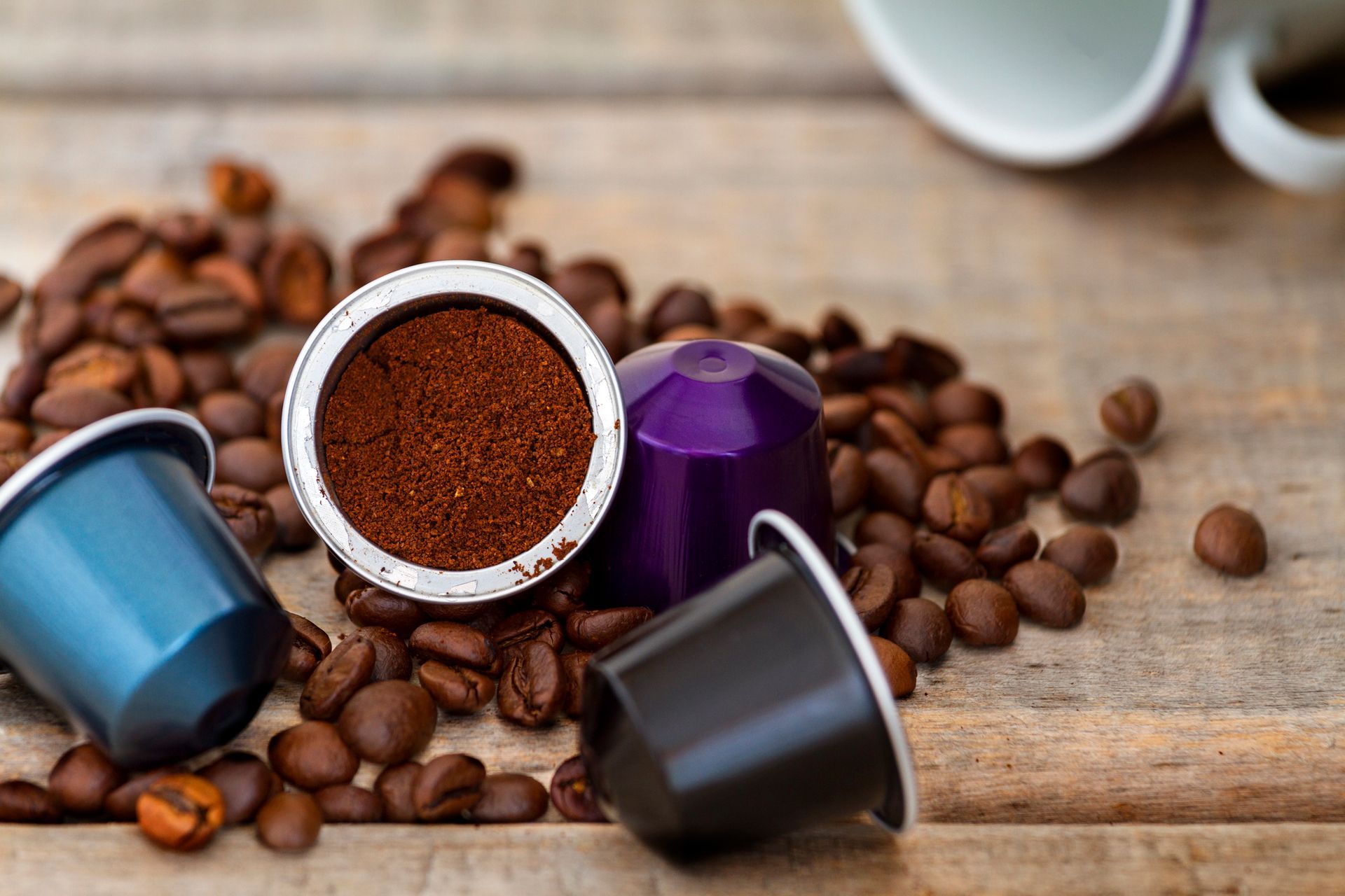 Capsule di caffè con caffè macinato, chicchi di caffè sparsi su una superficie di legno.