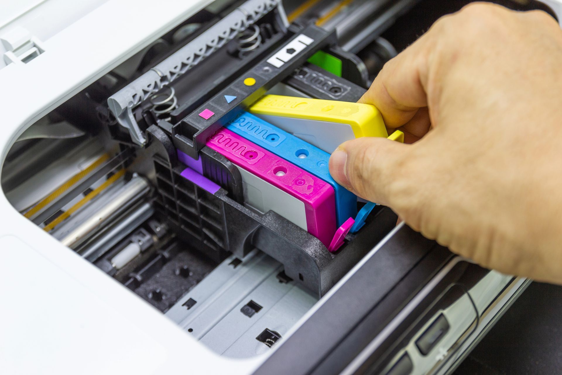 Inserimento manuale di una cartuccia di inchiostro giallo in una stampante con cartucce ciano, magenta e nero già inserite.