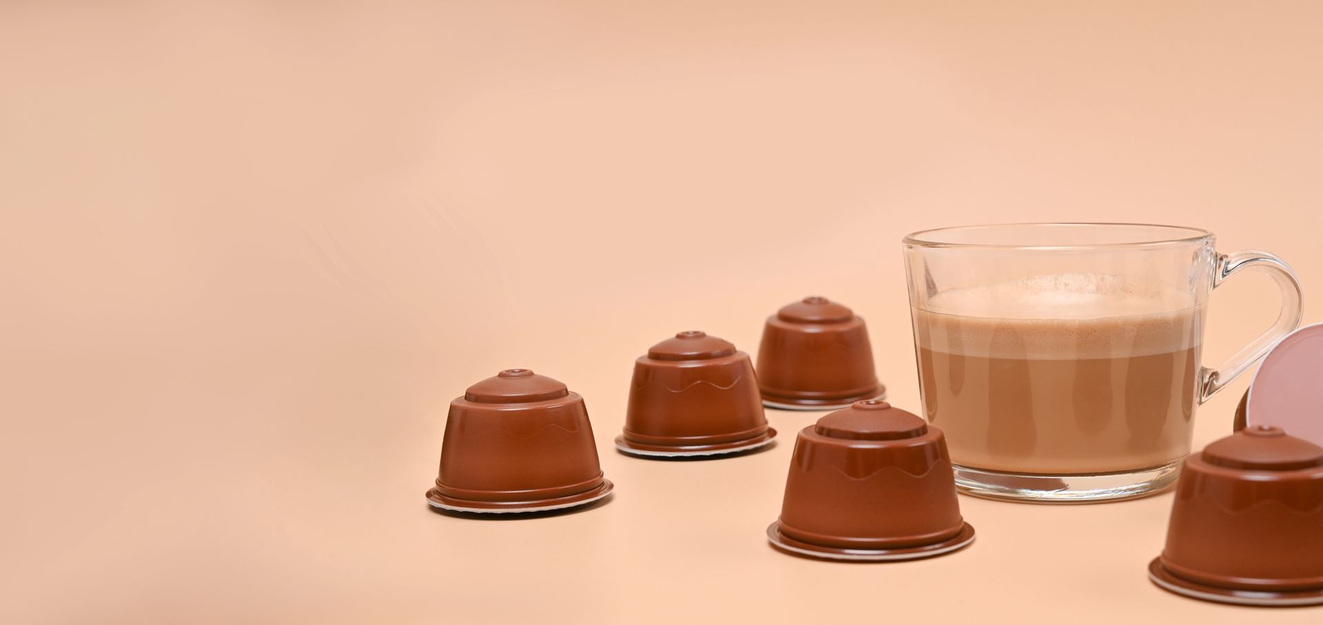 Capsule di caffè marrone sparse in una tazza di caffè su una superficie marrone chiaro.