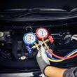 Gloved hand using red and blue AC manifold gauges on a car engine bay