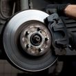 Close-up of a car brake rotor and caliper during repair, with a gloved hand holding the brake assembly.