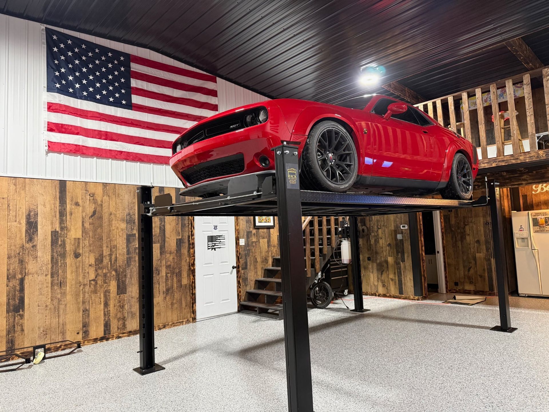 Red sports car on a lift in a garage with a large American flag on the wall