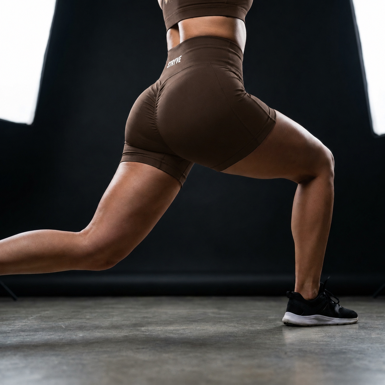 Person performing a lunge exercise in brown workout clothes on a gym floor against a dark background