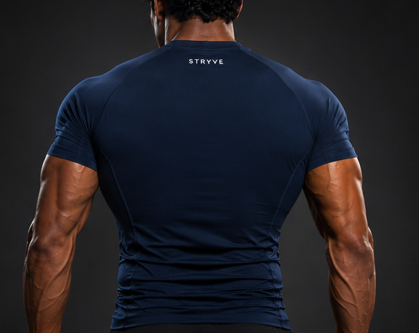 Muscular athlete in a navy fitted shirt standing with hands on hips against a dark background