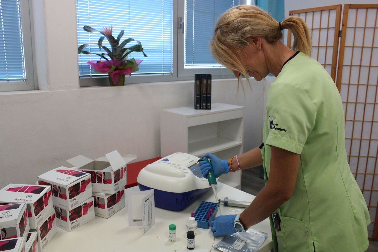 Un operatore sanitario in camice verde prepara il materiale necessario su un tavolo in una stanza della clinica.
