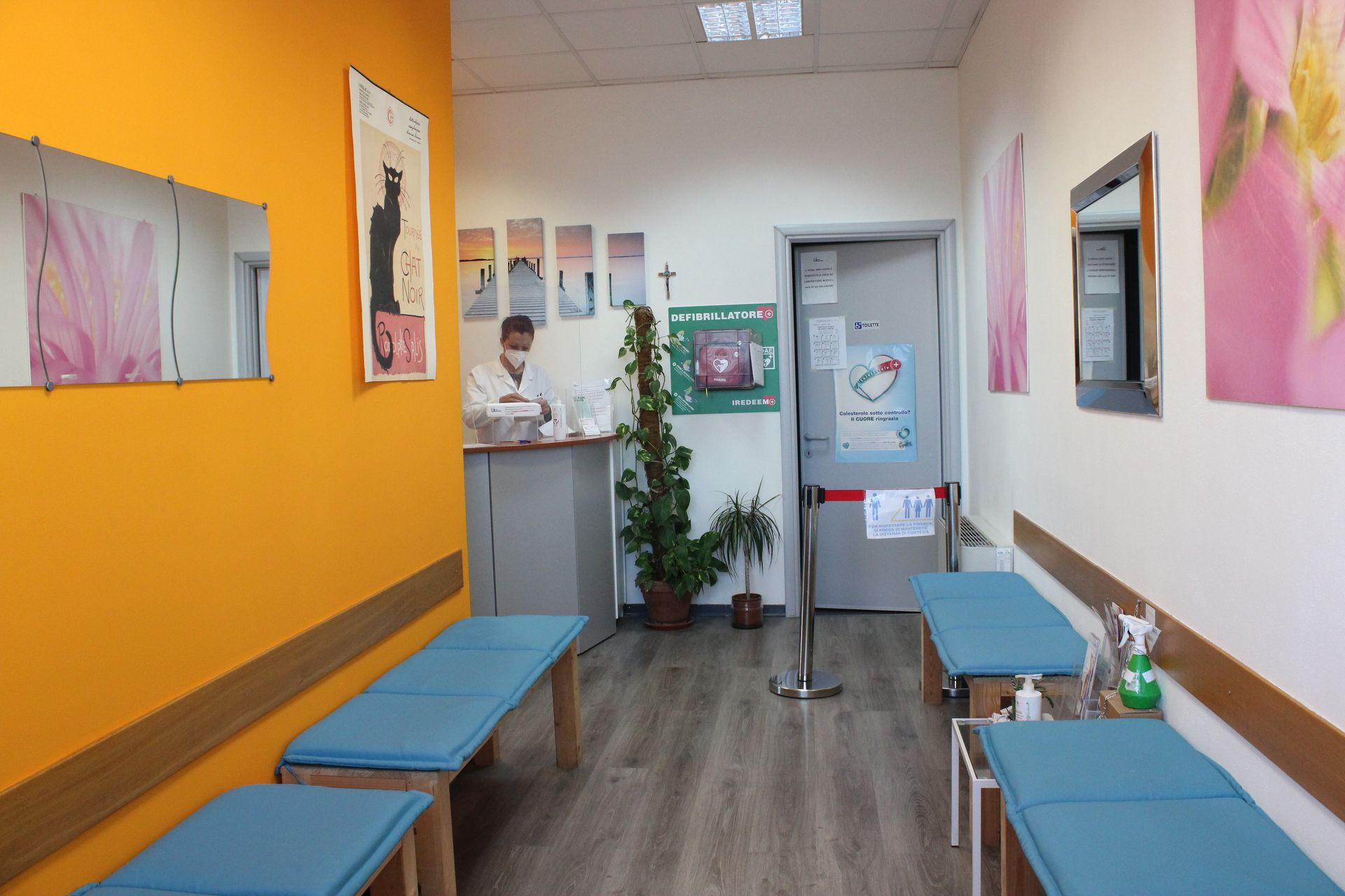 Sala d'attesa vuota con panchine blu, pareti arancioni e bianche e una porta sul retro.