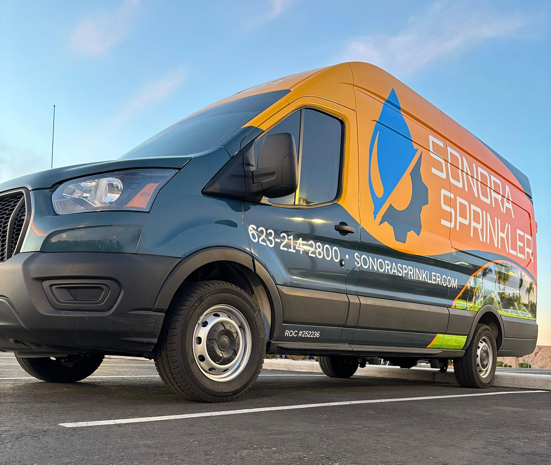 Green and yellow Sonora Sprinkler van parked in a parking lot.