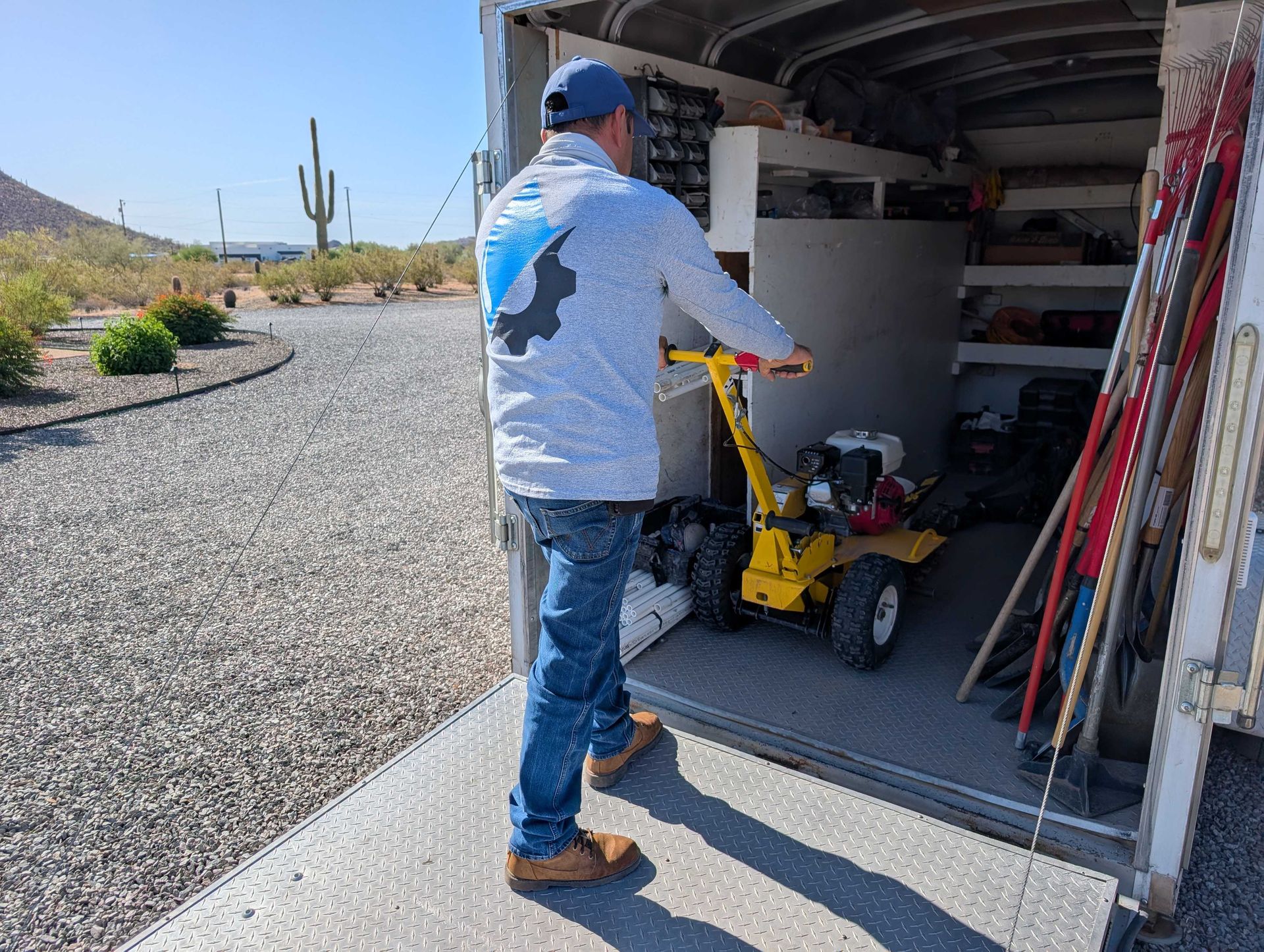Person using a yellow mower in a garage, with yard tools leaning nearby.