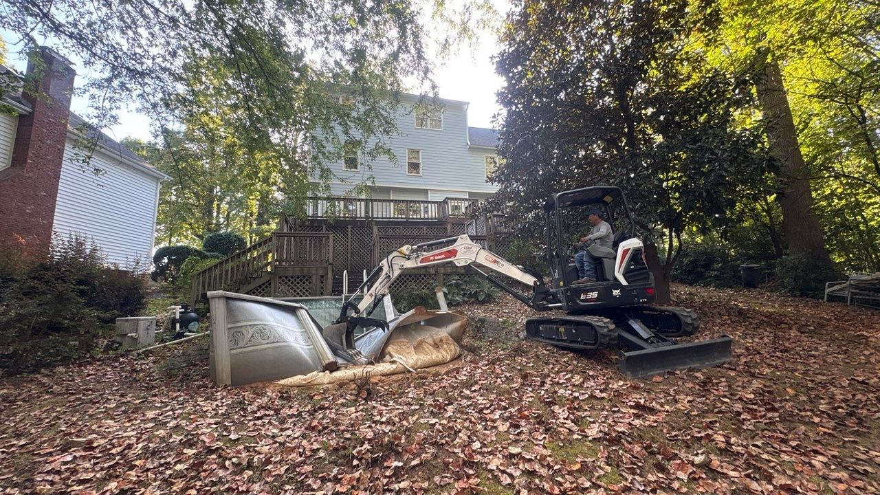 Bulldozer and debris in a leaf-covered backyard beneath a wooden deck after cleanup or demolition