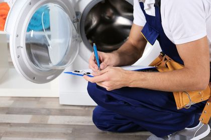 Técnico rellenando una lista de verificación junto a una lavadora de carga frontal abierta.