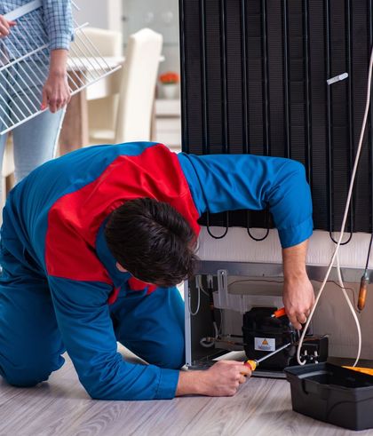 Un técnico se encuentra arrodillado junto a un equipo, utilizando una herramienta para reparar el cableado debajo de una máquina grande.