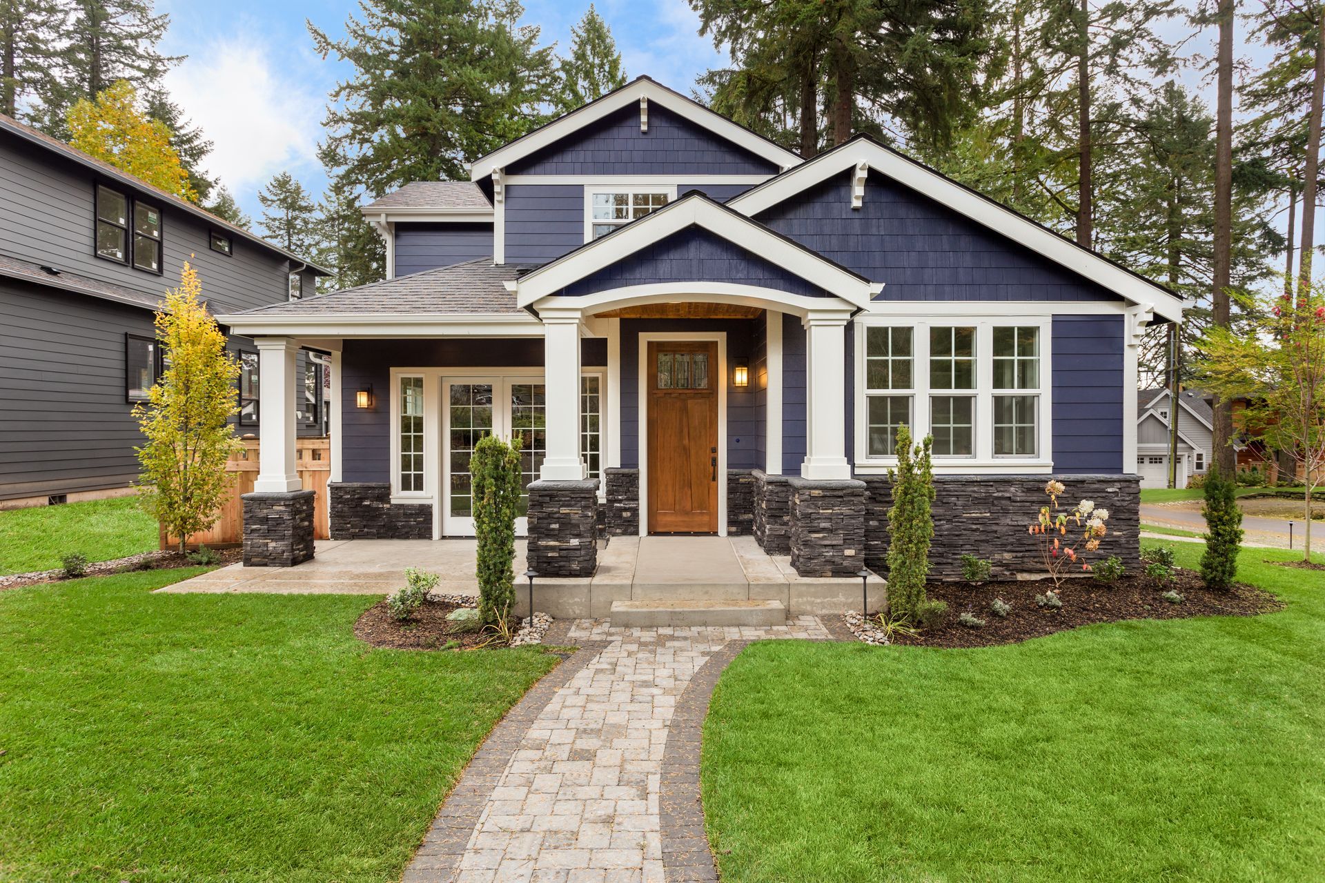 Blue-gray craftsman house with white trim, stone porch, and a curved walkway in a green yard