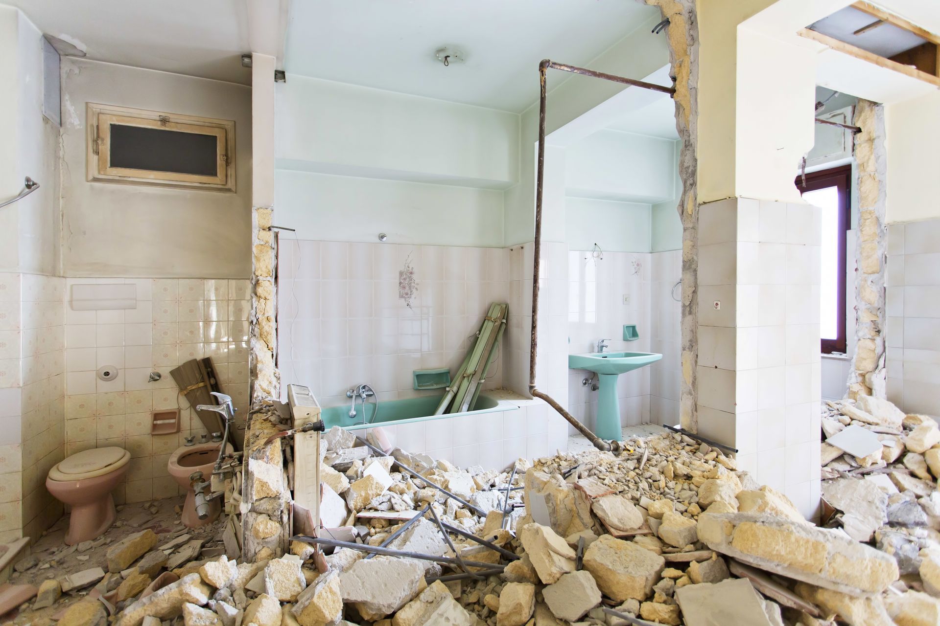 Partially demolished bathroom with rubble, broken walls, a bathtub, and a sink.