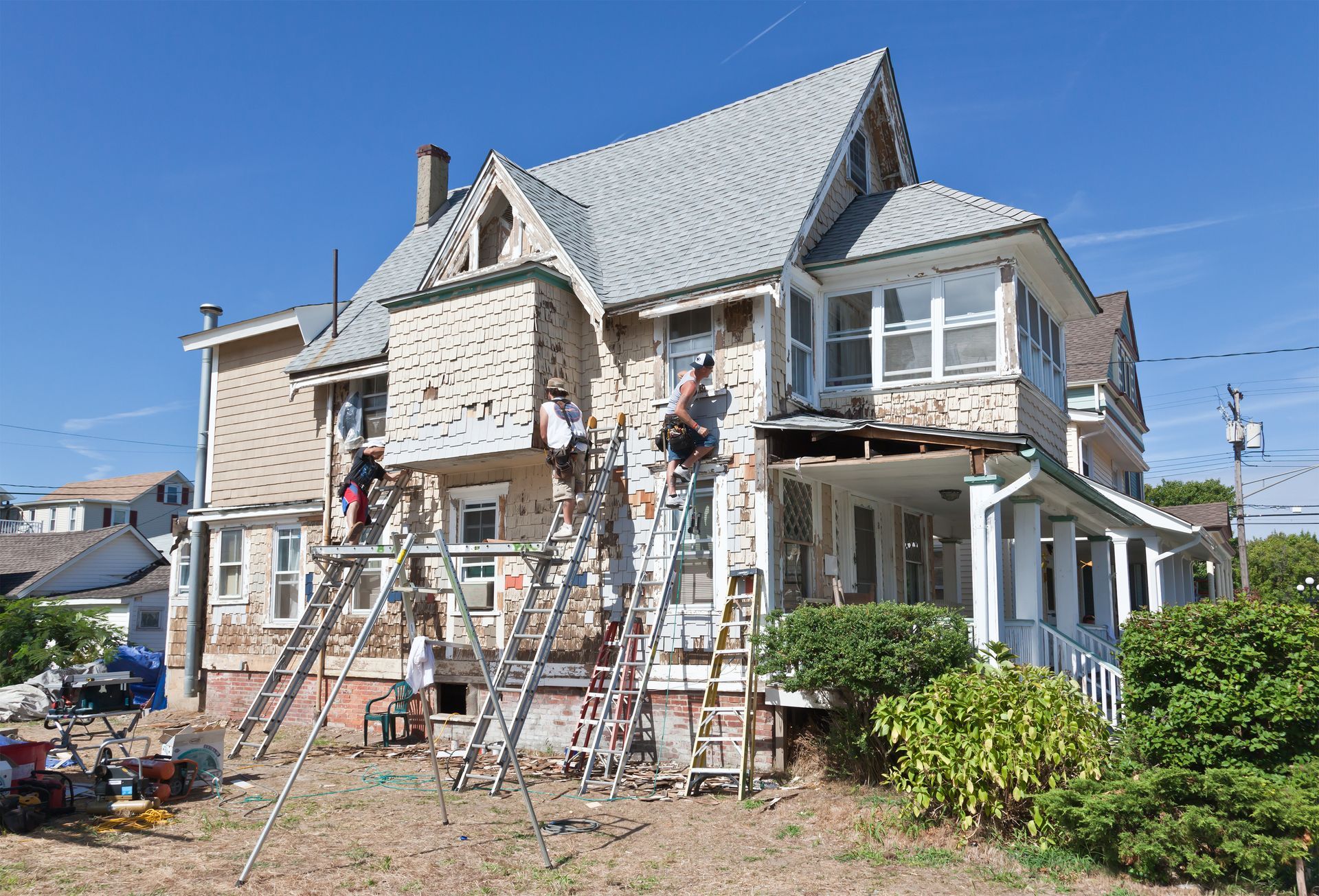 Workers on ladders repairing the siding and roof of a two-story house on a sunny day