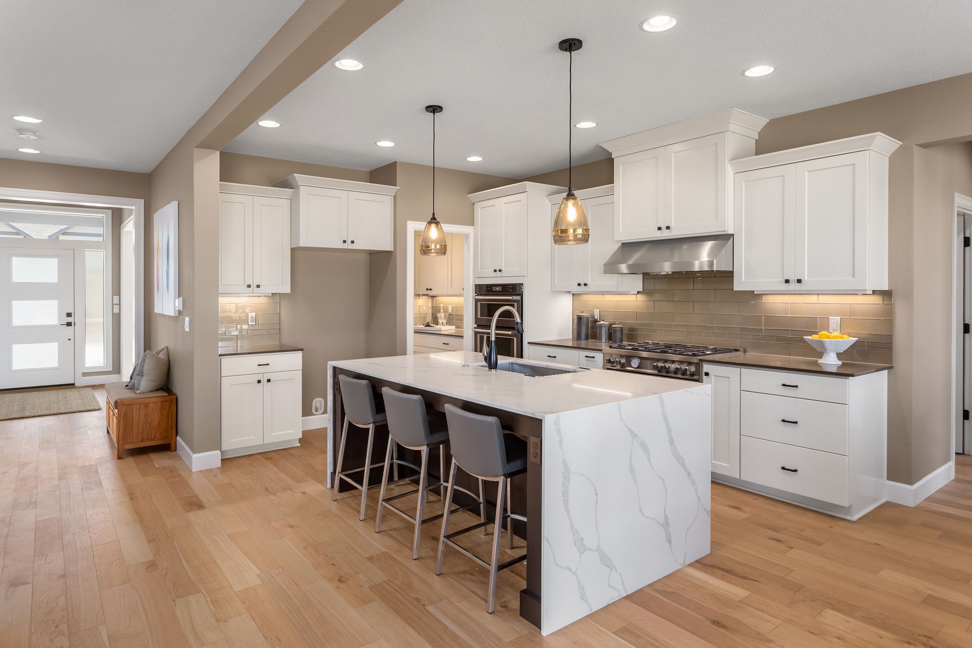 Bright modern kitchen with white cabinets, marble island, pendant lights, and light wood floors