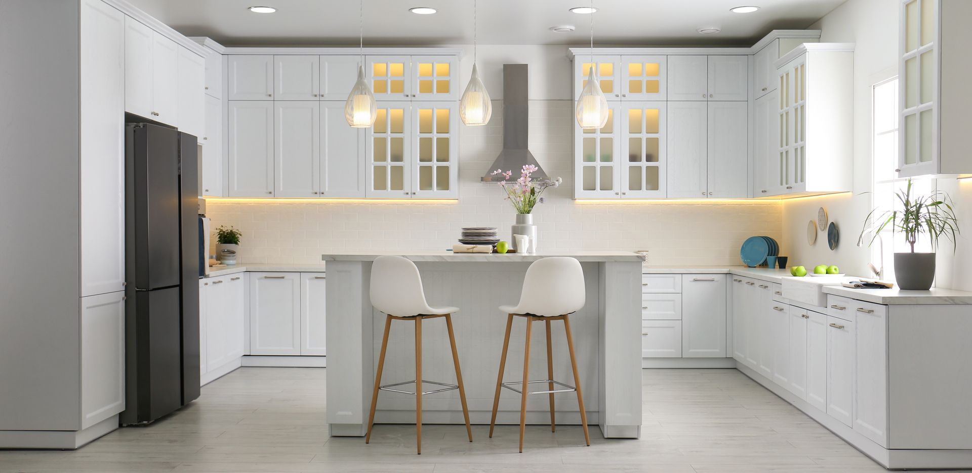Bright modern white kitchen with island, bar stools, cabinets, and warm under-cabinet lighting