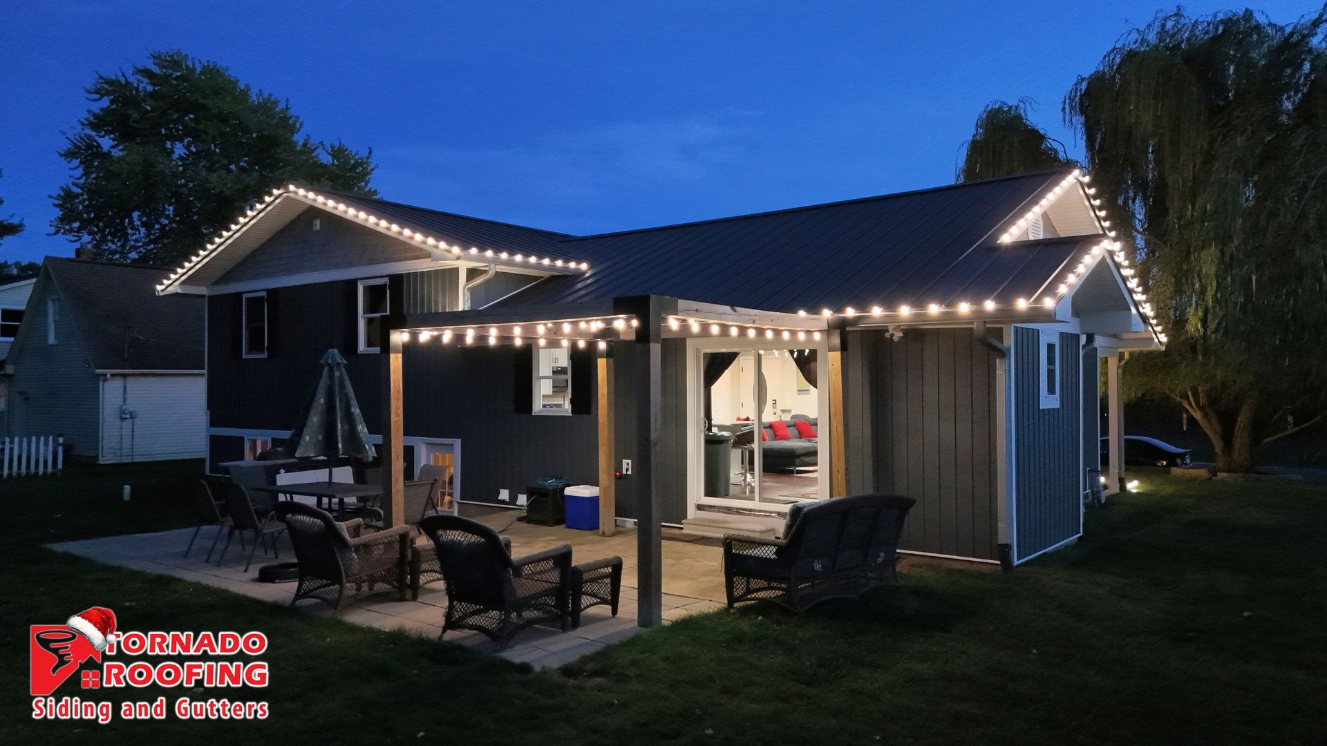 House exterior lit with string lights at dusk. Patio furniture on a stone patio.