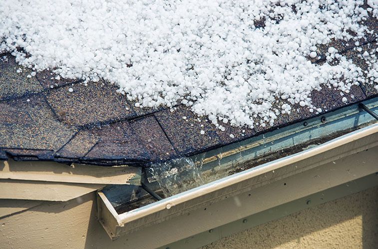 Hail covering a dark shingled roof and overflowing into the gutter.