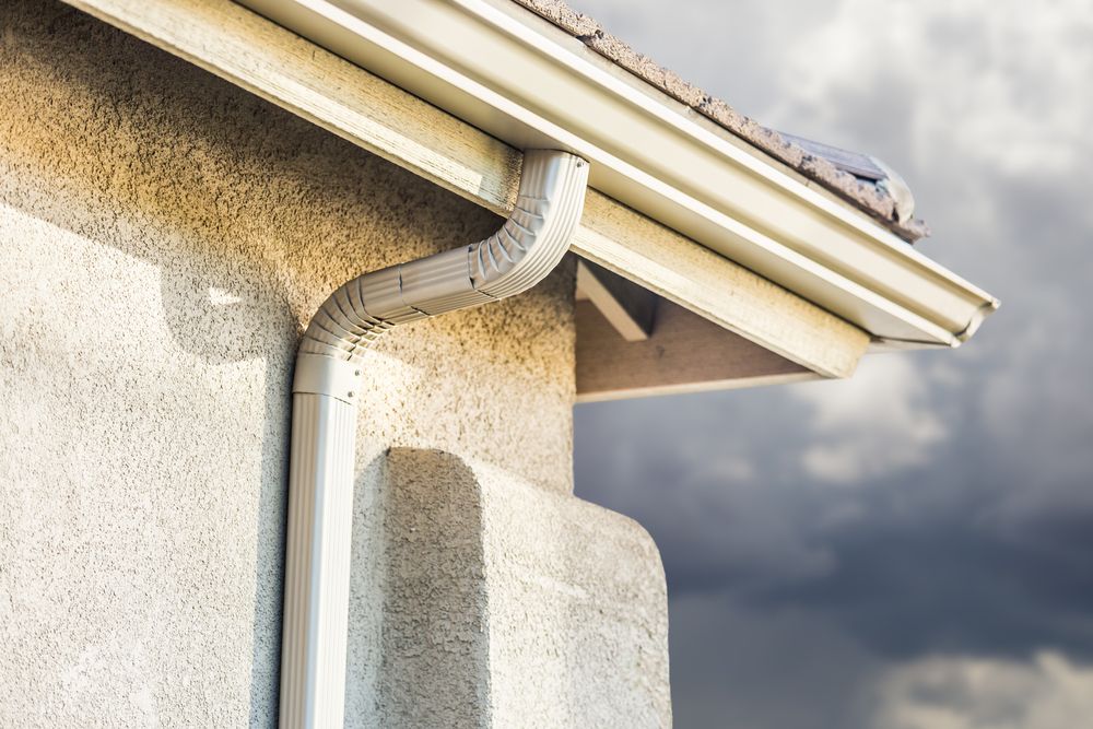 White gutter system on a stucco house against a cloudy sky.