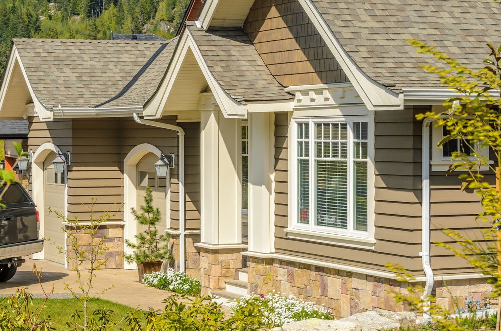 Brown-sided house with white trim, arched garage, stone accents, and multi-paned window.