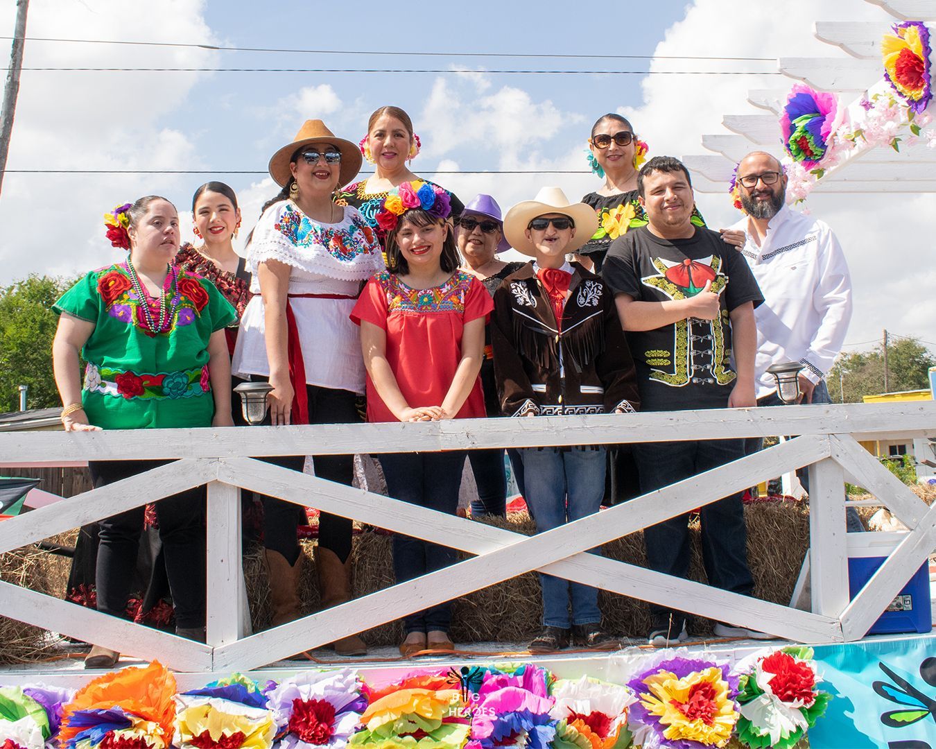 Group of people smiling on a decorated float; many wear colorful Mexican clothing and hats.