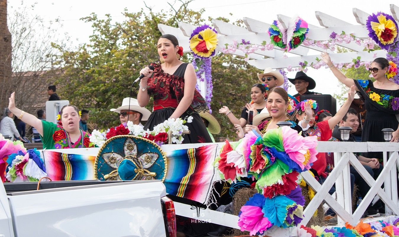 People in colorful dresses on a decorated float, celebrating. Bright colors, outdoor setting, and joyful expressions.