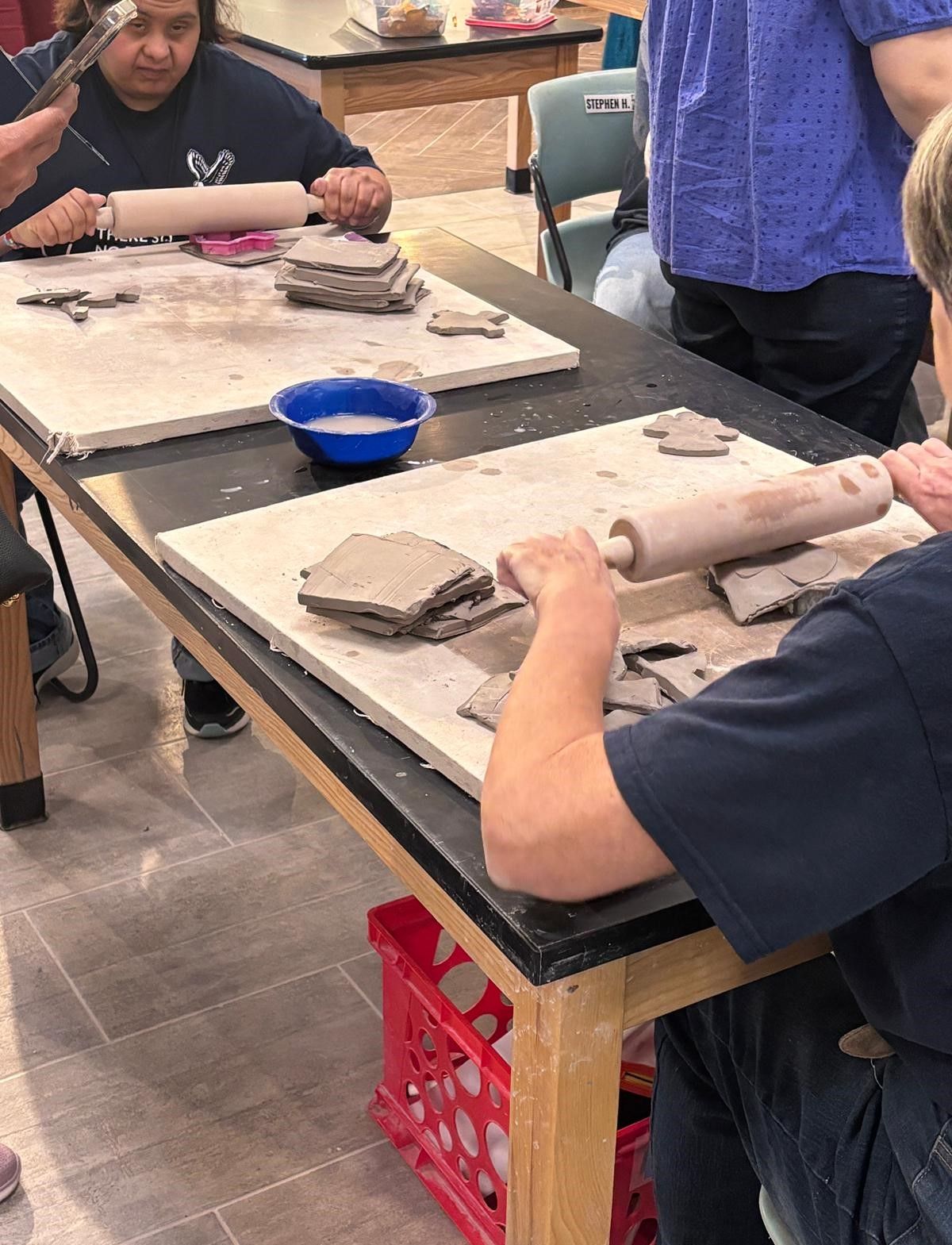 A group of people are sitting at a table rolling clay.