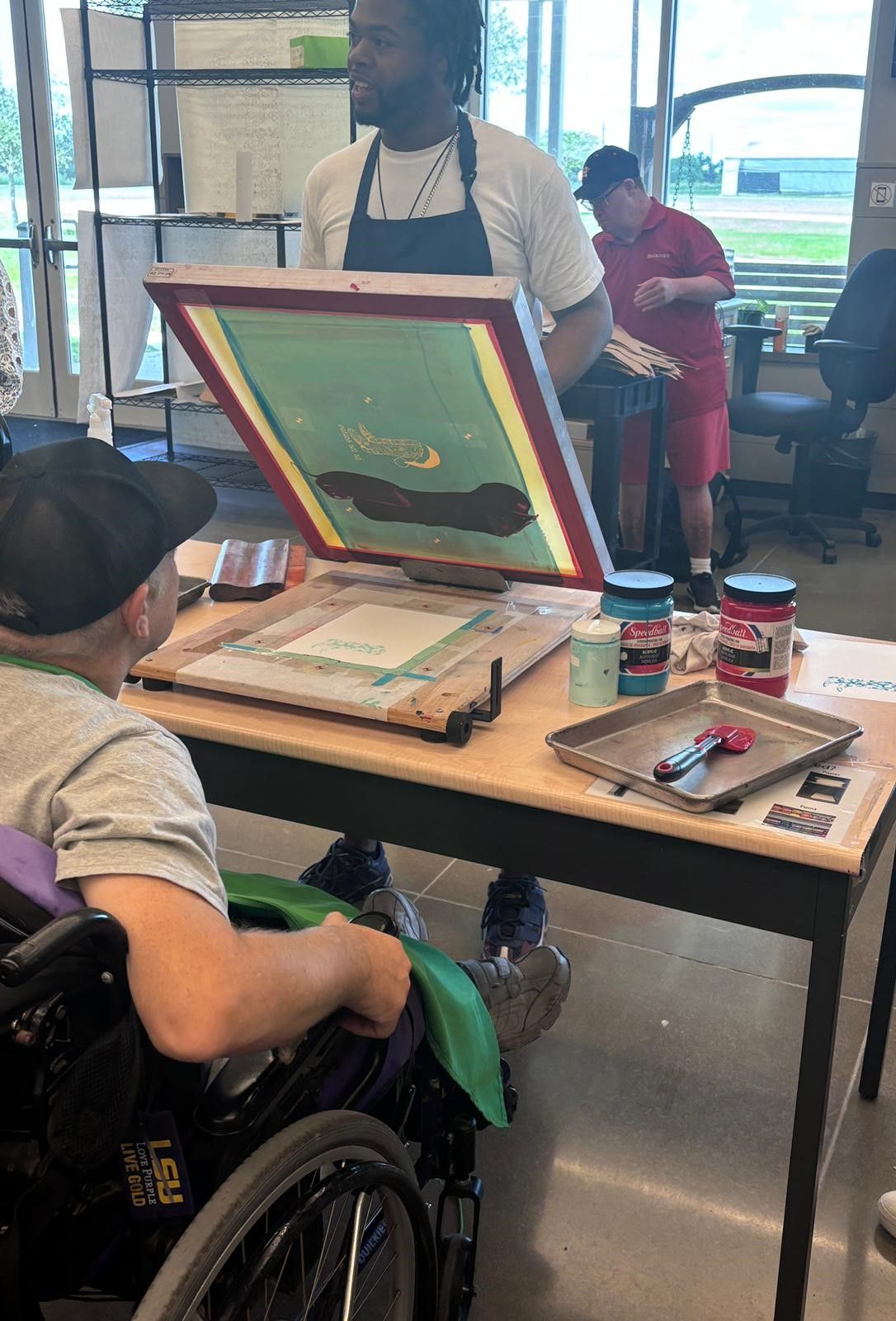 A man in a wheelchair is sitting at a table with a screen printing machine.