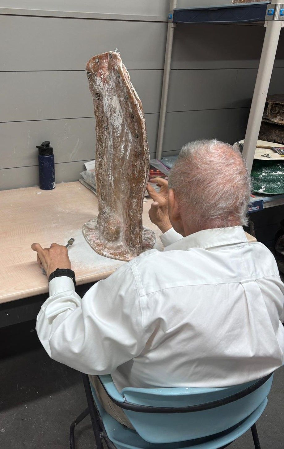 A man is sitting at a desk looking at a statue.