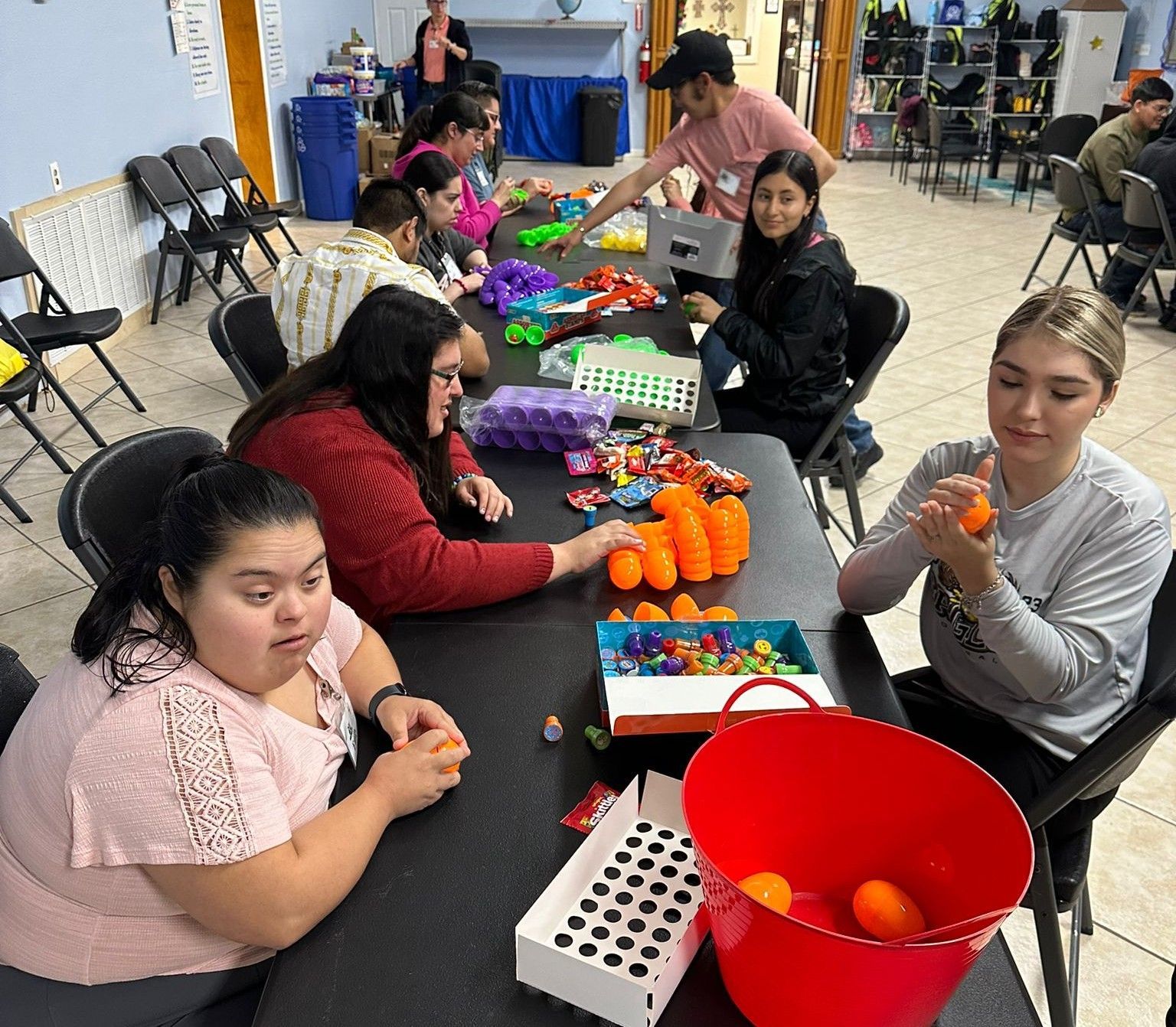 People sitting at a table filling Easter eggs, likely for an event. Inside a room.