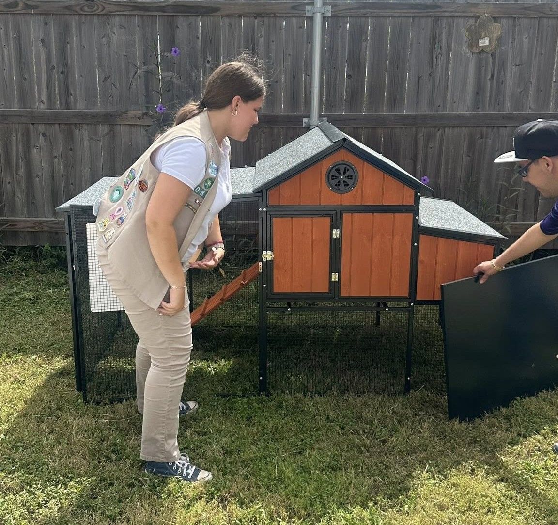 Two people assembling a brown and black chicken coop in a grassy yard.