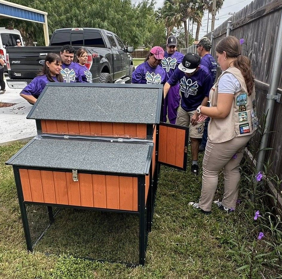 Group of people building a chicken coop outdoors; woman pointing at the open door.