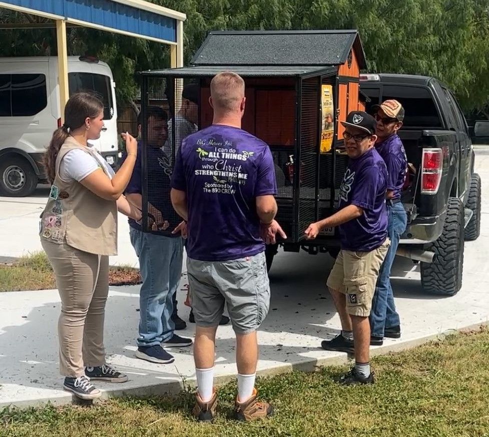Group of people loading a wooden structure into a pickup truck on a sunny day.