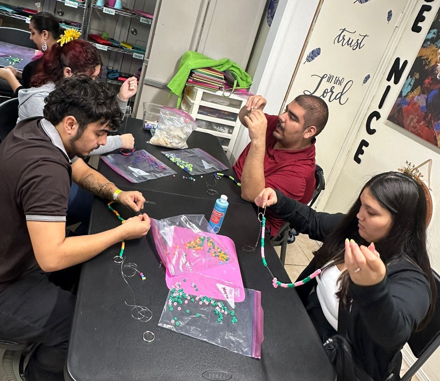 People making jewelry at a table, beads and string visible.