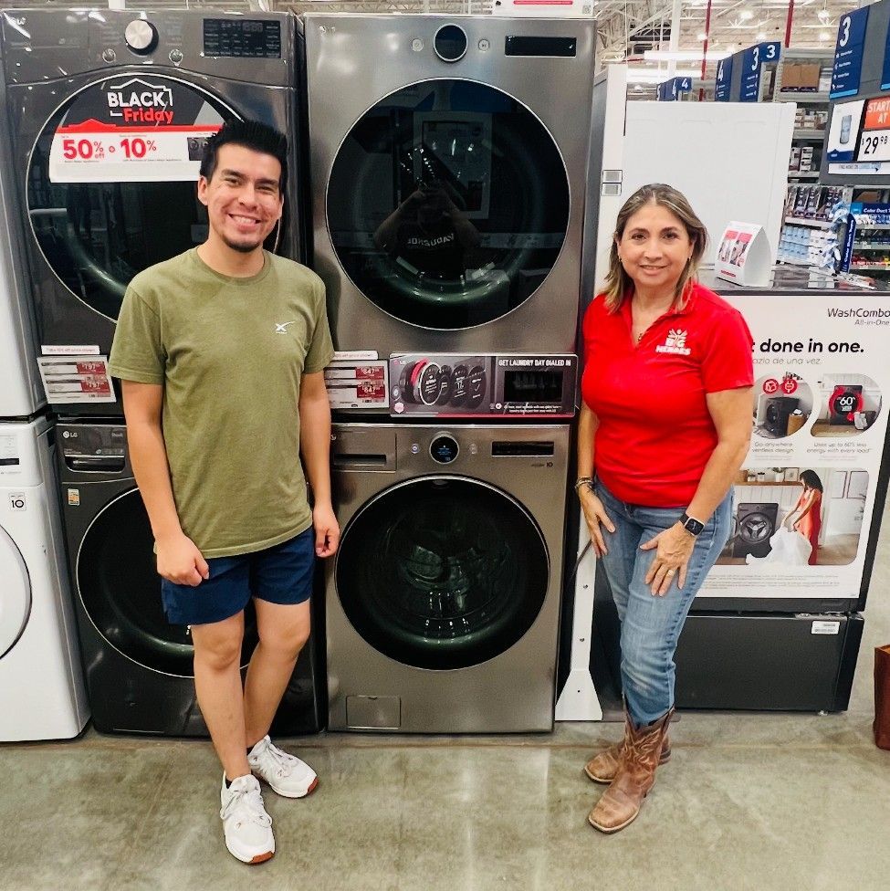 Two people stand beside a stacked washer and dryer in a store.