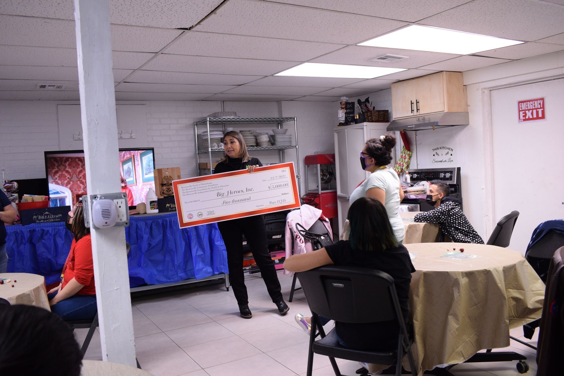 Woman holding sign in room with people at tables.