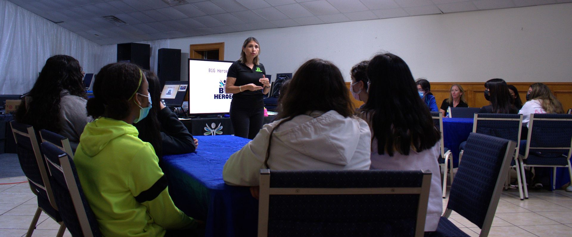 A woman giving a presentation to a group seated around a table in a room.