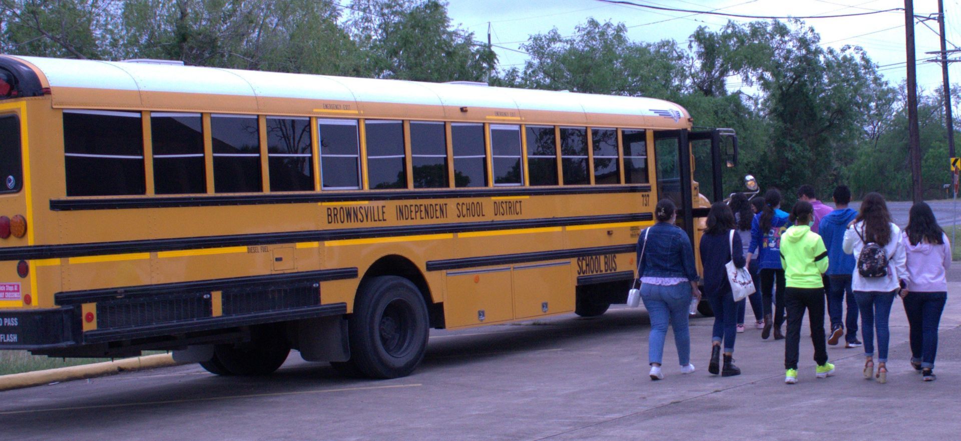 A yellow school bus with students boarding, outdoors.