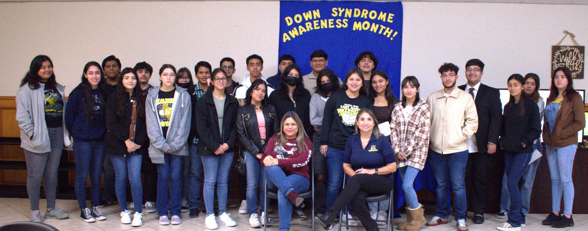 Group of students and adults pose for a photo in front of a banner that says 