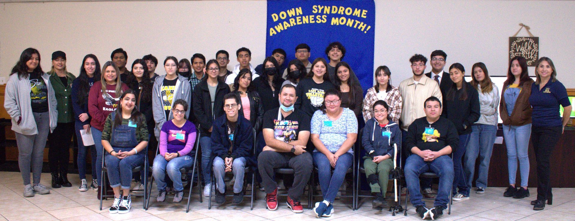 Group photo celebrating Dawn Sparrows Awareness Month. People are seated and standing, smiling, near a blue banner.