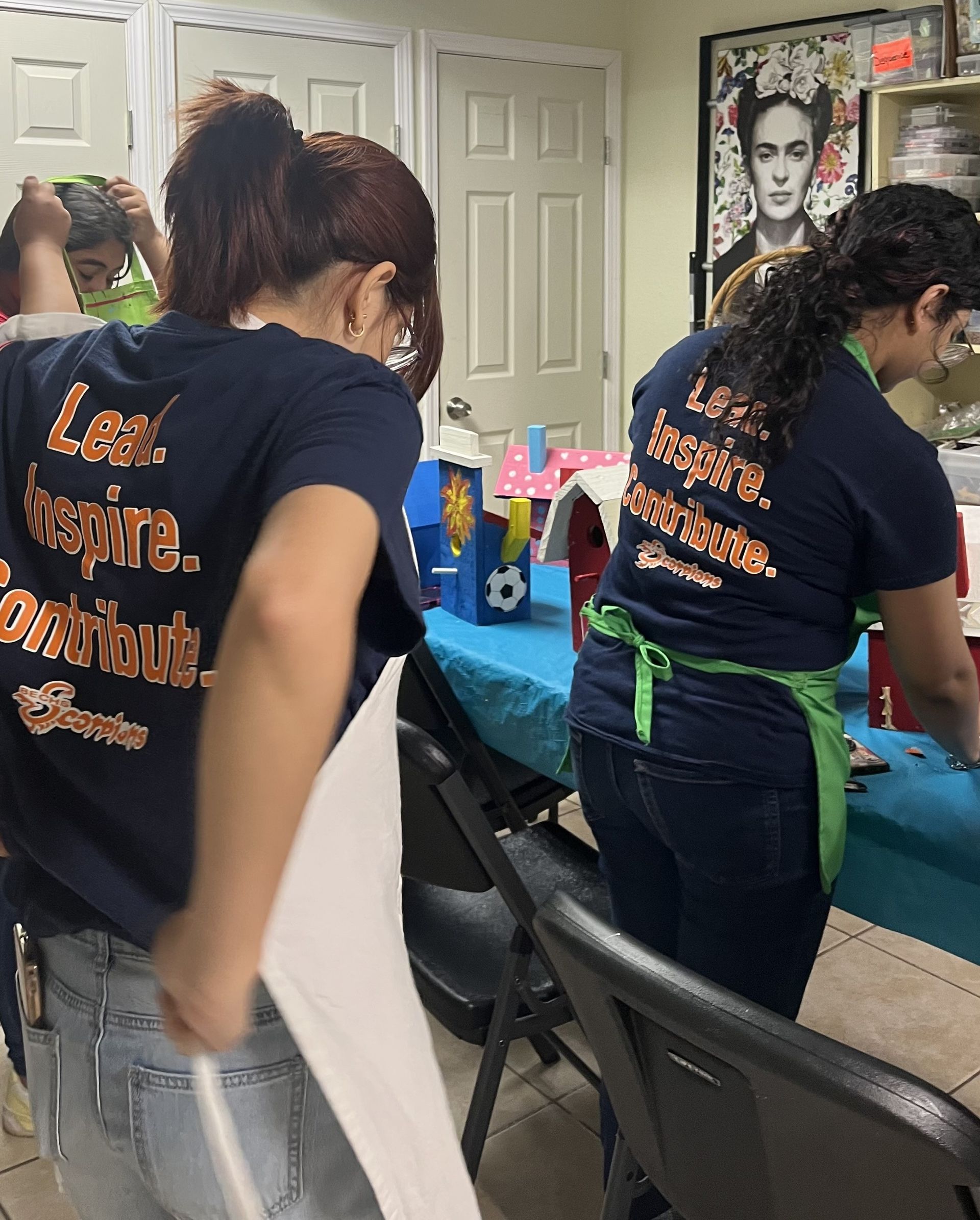 3 people, backs to the camera, in blue shirts that say 