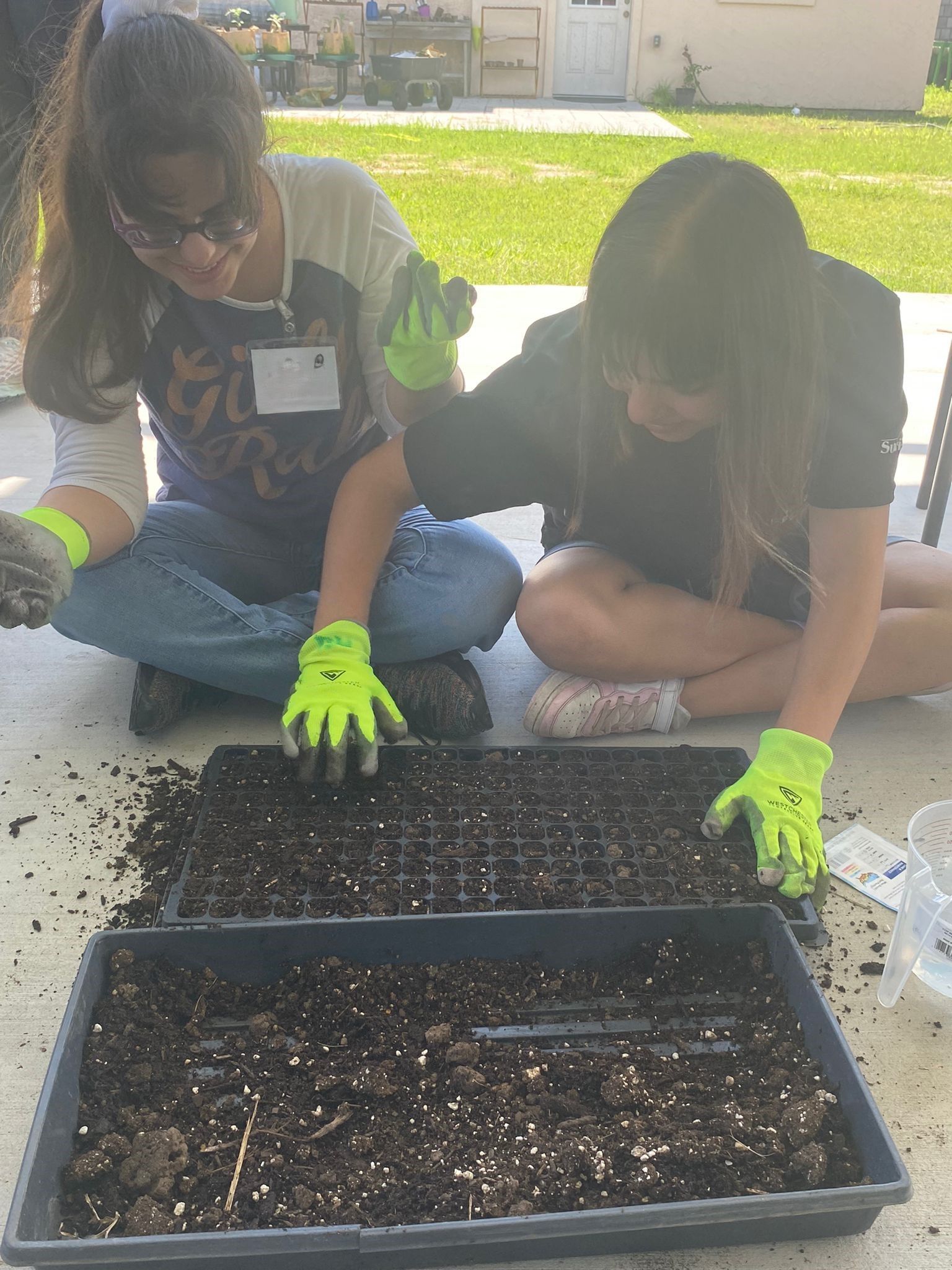 Two girls are sitting on the ground working on a tray of dirt.