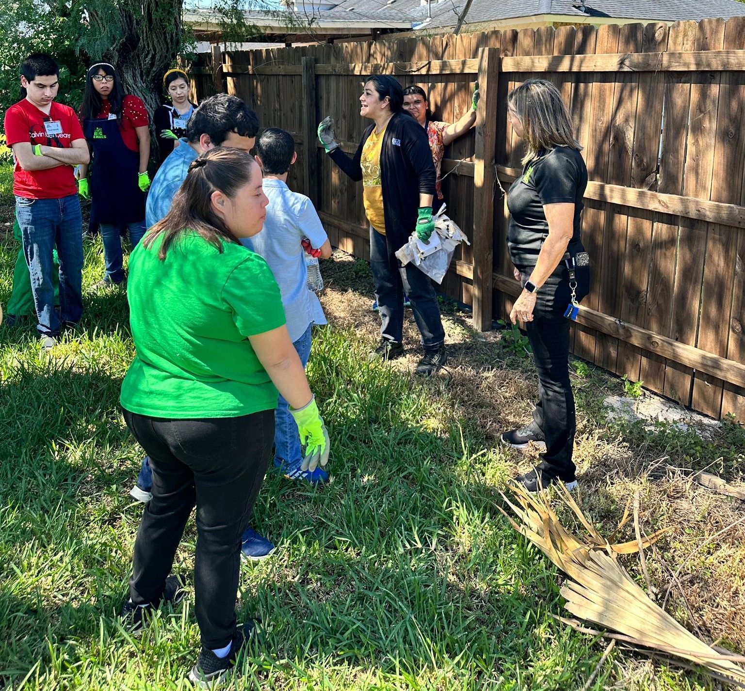 A group of people are standing in front of a wooden fence.