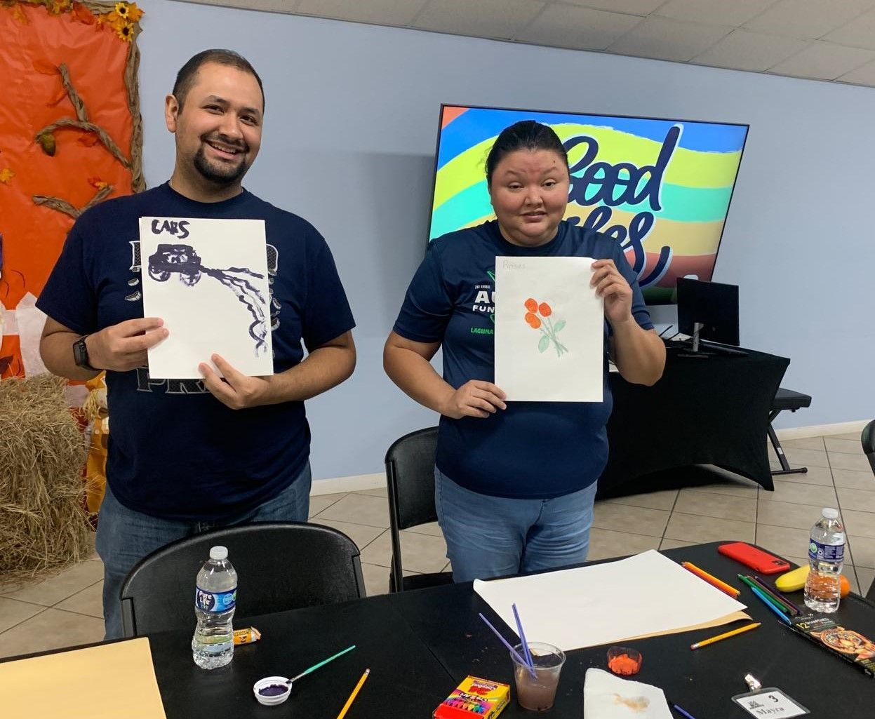 A man and a woman are standing next to each other holding up their paintings.