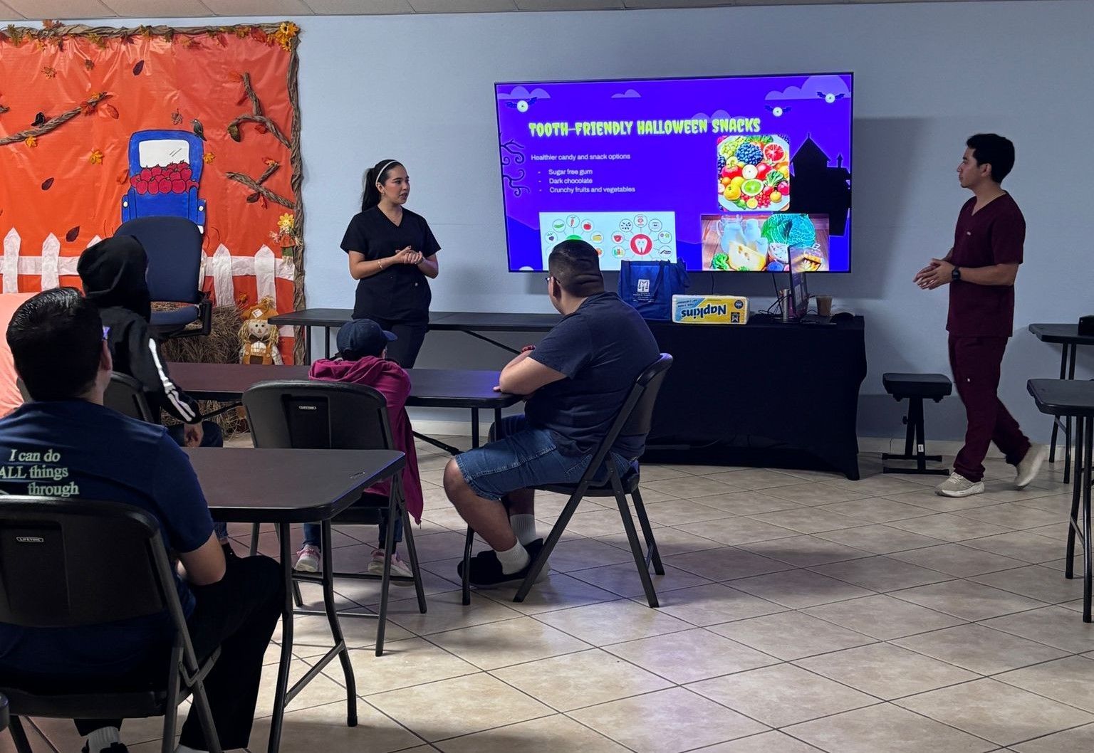 A woman is giving a presentation to a group of people sitting at tables.