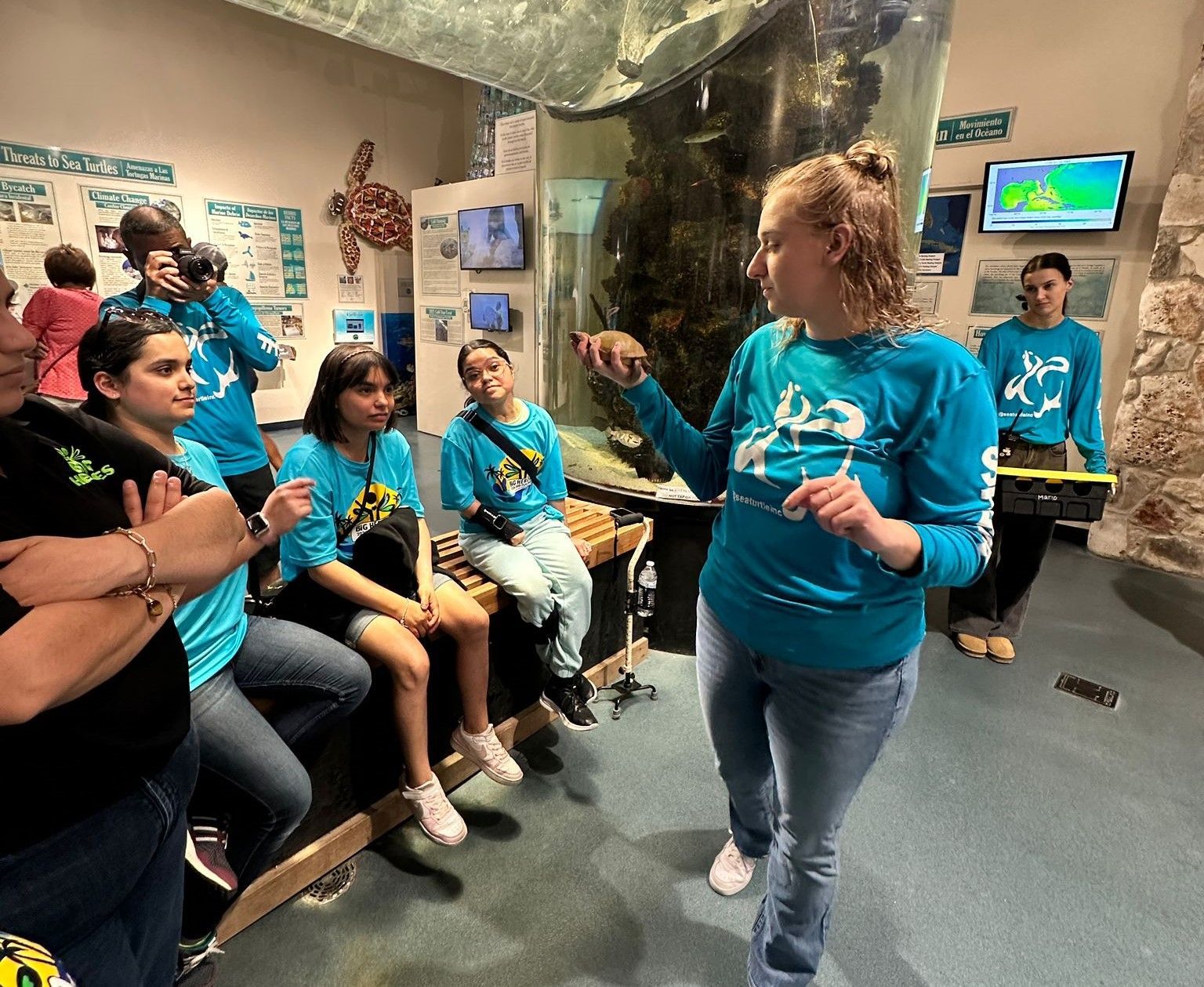 A woman in a blue shirt is talking to a group of people