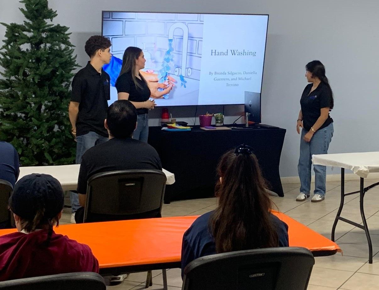 A presentation on a screen with people looking on. One person gestures at the screen, presenting to the audience.