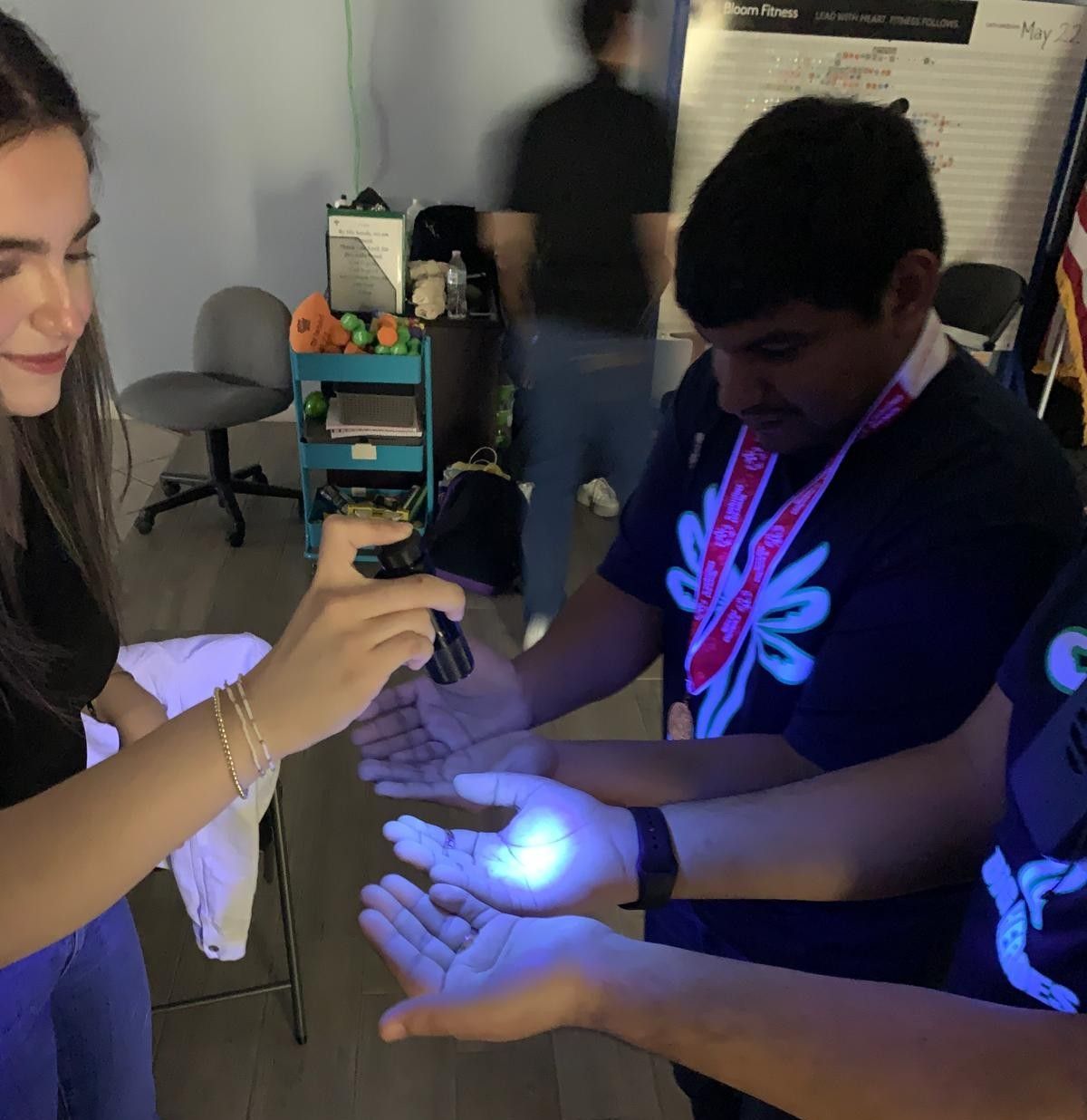Woman shining UV light on hands of two men, illuminating a glow indoors.