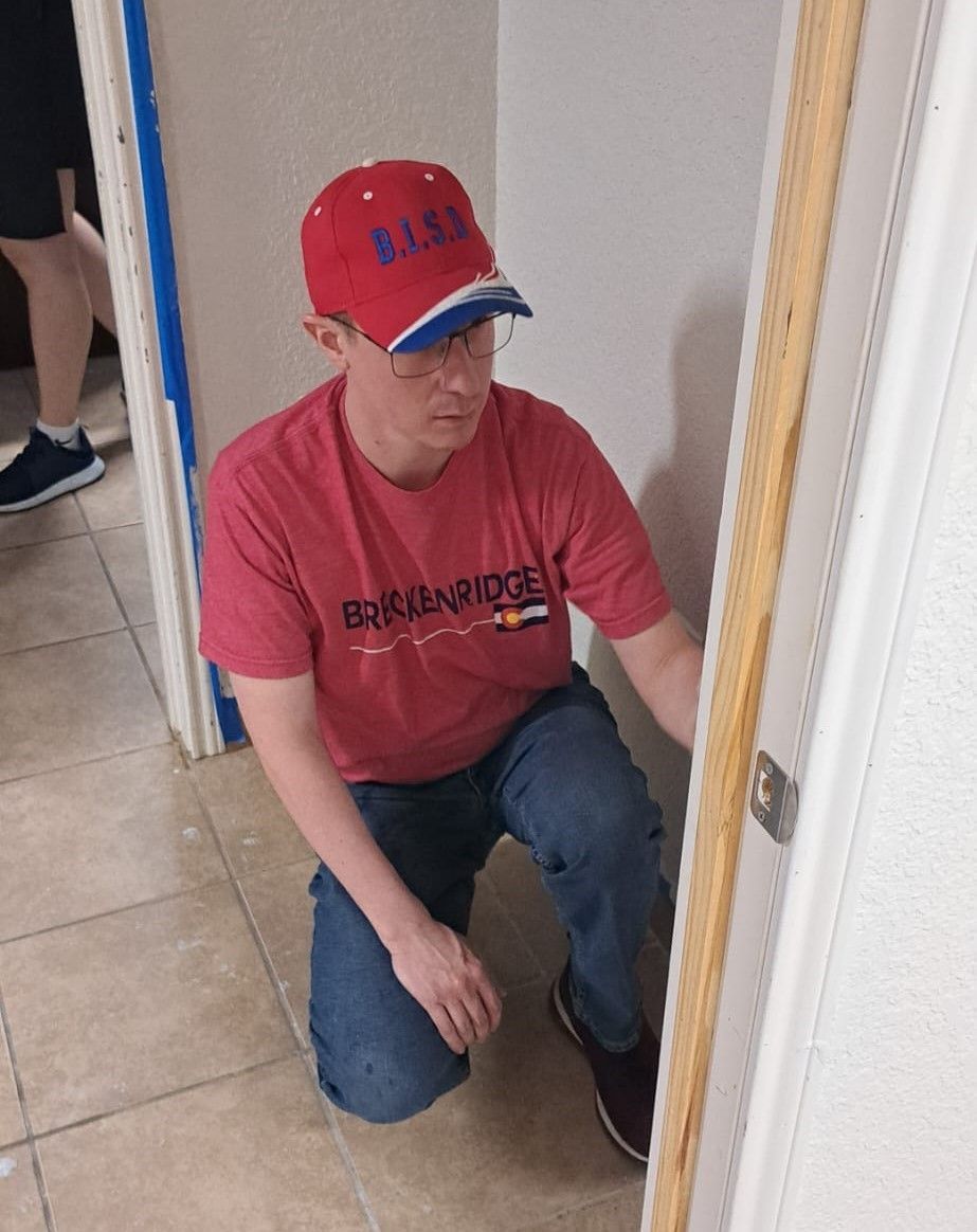 A man wearing a red shirt and a red hat is kneeling next to a door