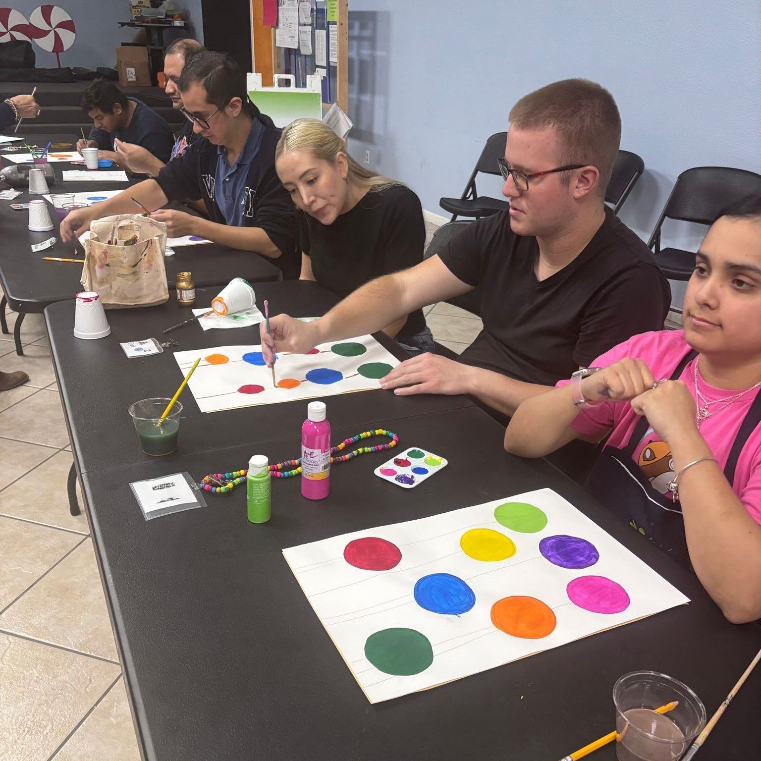 A group of people are sitting at a table painting